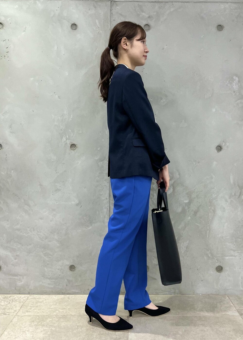 ブラック系のパンプス、ブルー系のスラックス、ブラック系のトートバッグを着用したレディースの春コーディネートの2枚目の写真