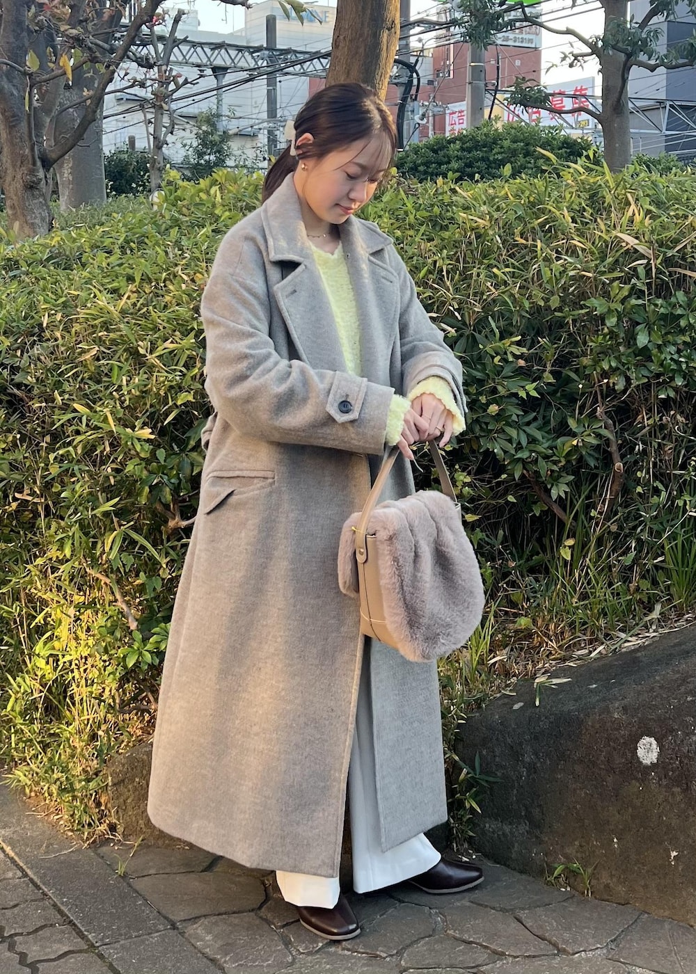 ベージュ系のチェスターコート、ブラウン系のショルダーバッグ、イエロー系のニット/セーターを着用したレディースの秋コーディネートの4枚目の写真