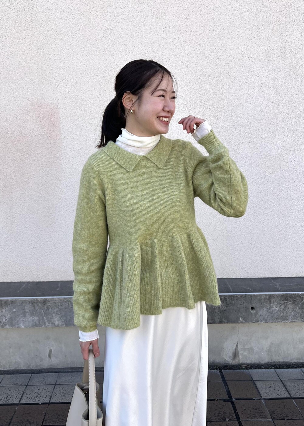 ホワイト系のスカート、グリーン系のニット/セーター、ベージュ系のパンプスを着用したレディースの冬コーディネートの7枚目の写真