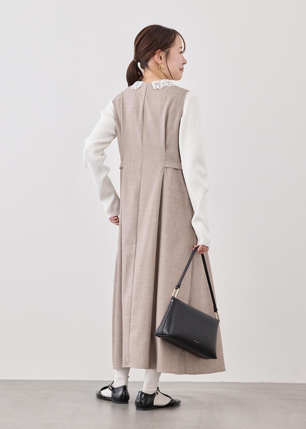 ブラック系のショルダーバッグ、ホワイト系のニット/セーター、ベージュ系のジャンパースカートを着用したレディースの春コーディネートの5枚目の写真