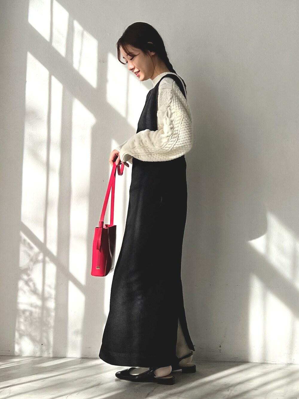 ブラック系のジャンパースカート、ホワイト系のニット/セーター、ピンク系のショルダーバッグを着用したレディースの冬コーディネートの2枚目の写真