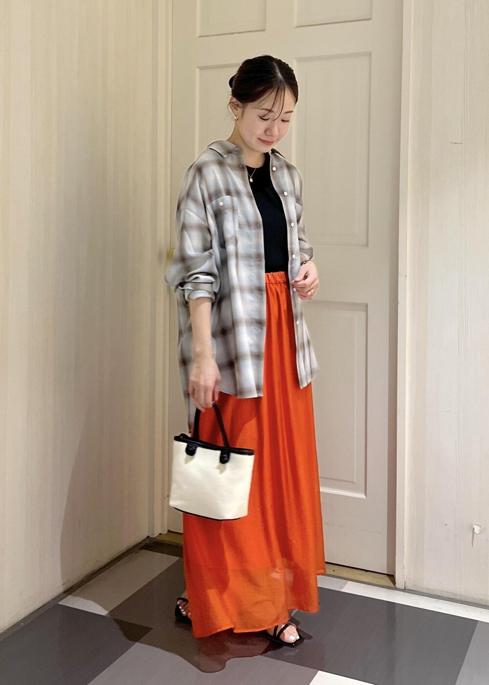 オレンジ系のスカート、ブラック系のタンクトップ、ブラック系のサンダルを着用したレディースの夏コーディネートの2枚目の写真