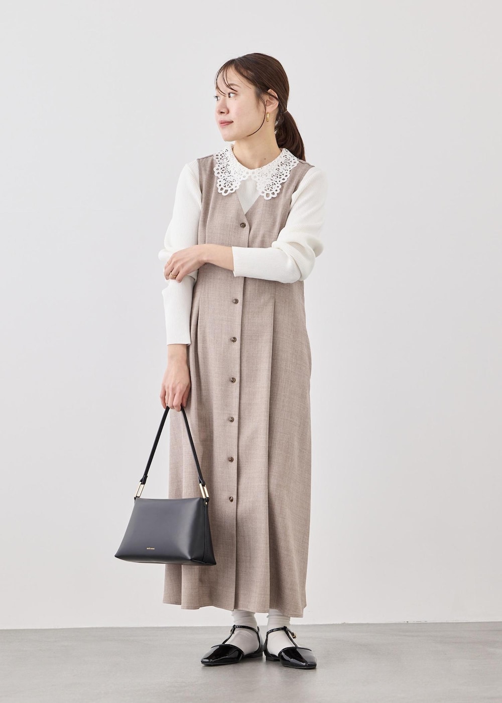 ブラック系のショルダーバッグ、ホワイト系のニット/セーター、ベージュ系のジャンパースカートを着用したレディースの春コーディネートの4枚目の写真