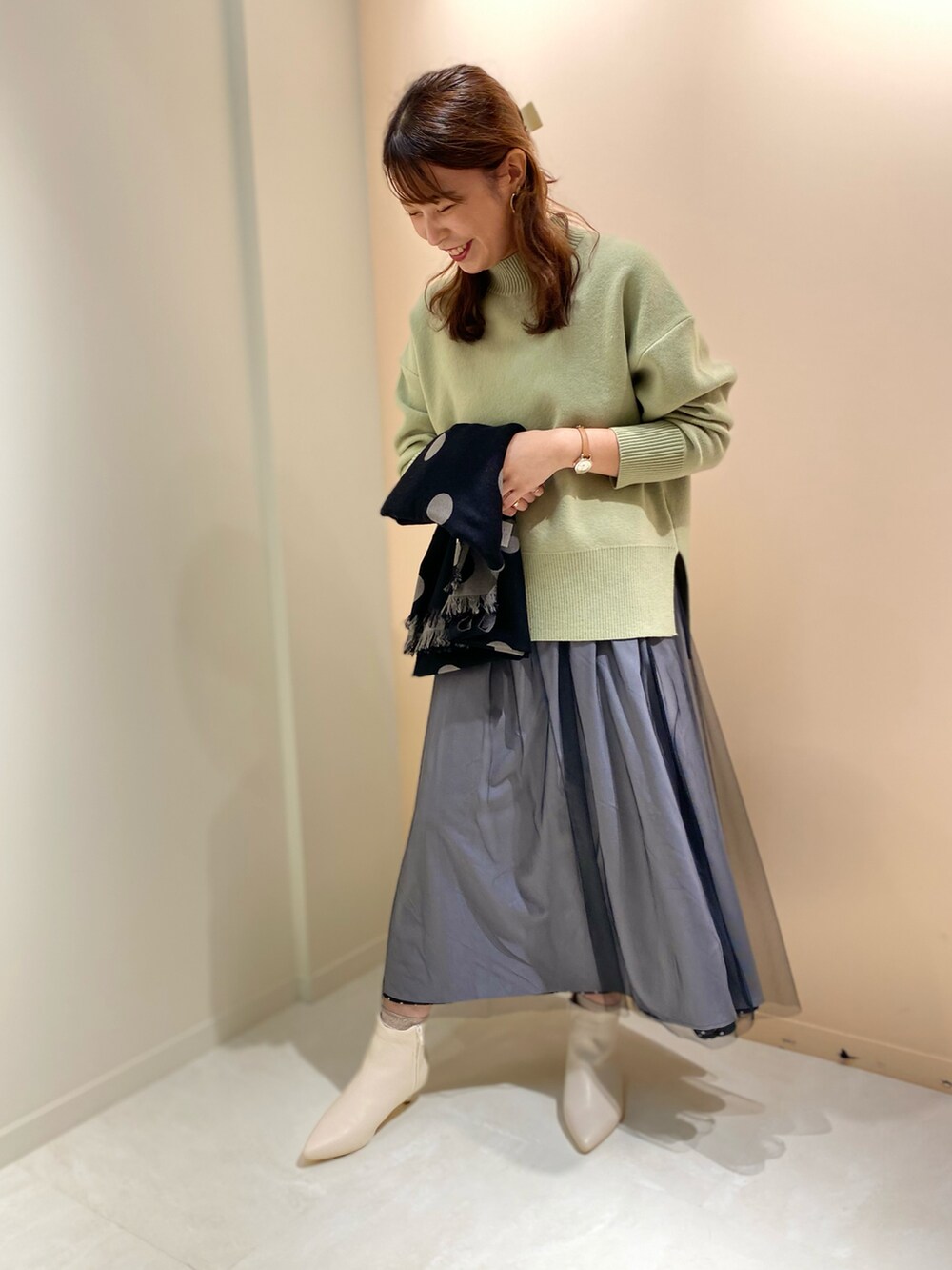 グリーン系のニット/セーター、ホワイト系のブーツ、ブラック系のストール/ショールを着用したレディースの冬コーディネートの2枚目の写真