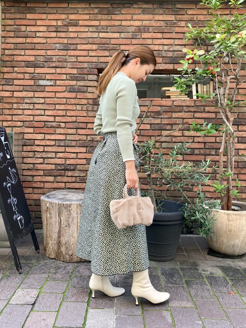 ブラック系のスカート、ベージュ系のハンドバッグ、ホワイト系のブーツを着用したレディースの秋コーディネートの2枚目の写真