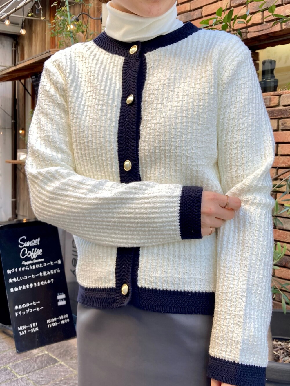 ホワイト系のカーディガン/ボレロ、グレー系のスカート、ブラック系のブーツを着用したレディースの冬コーディネートの2枚目の写真