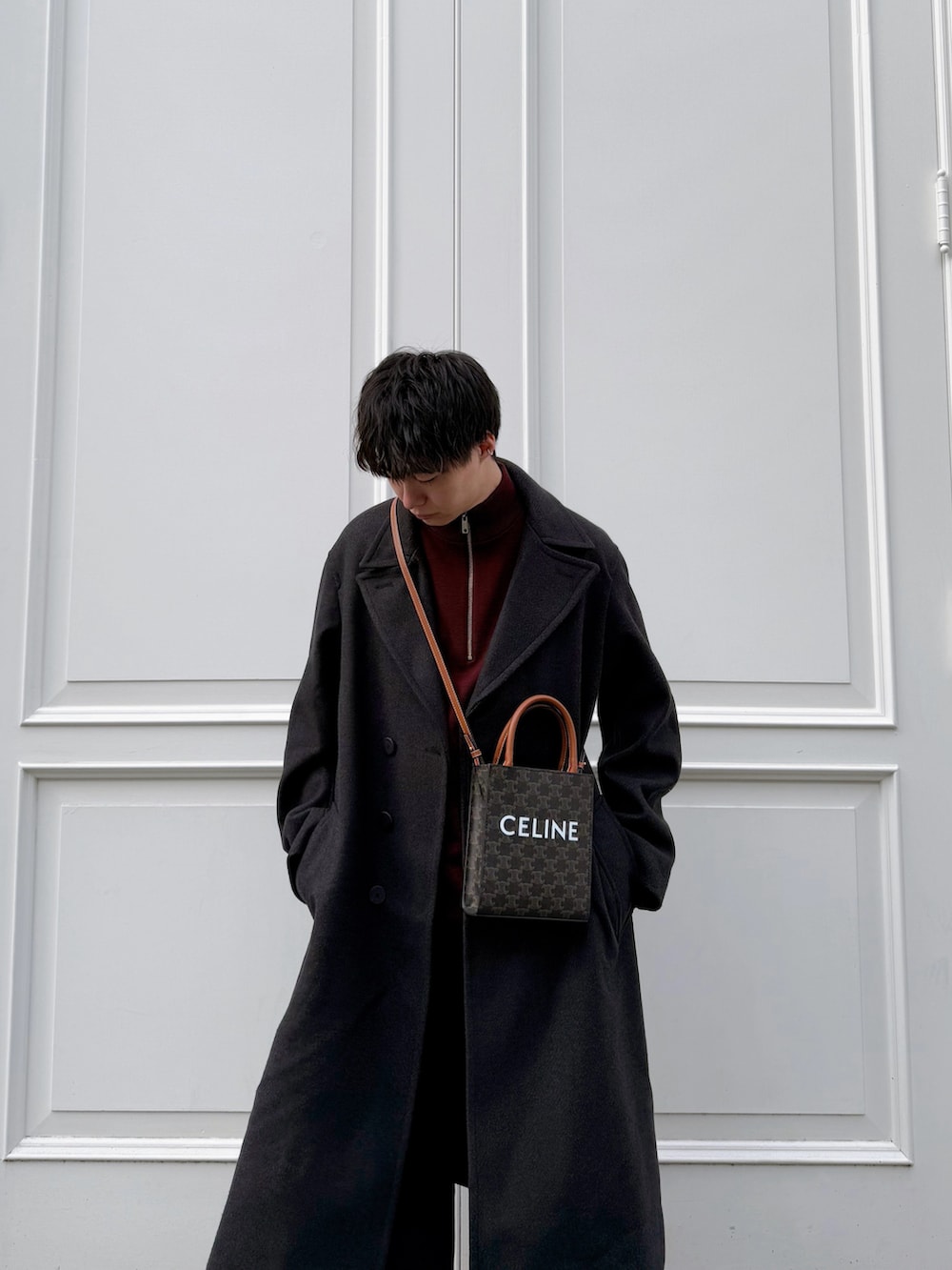 グレー系のチェスターコート、レッド系のニット/セーター、ブルー系のデニムパンツを着用したメンズの冬コーディネートの3枚目の写真