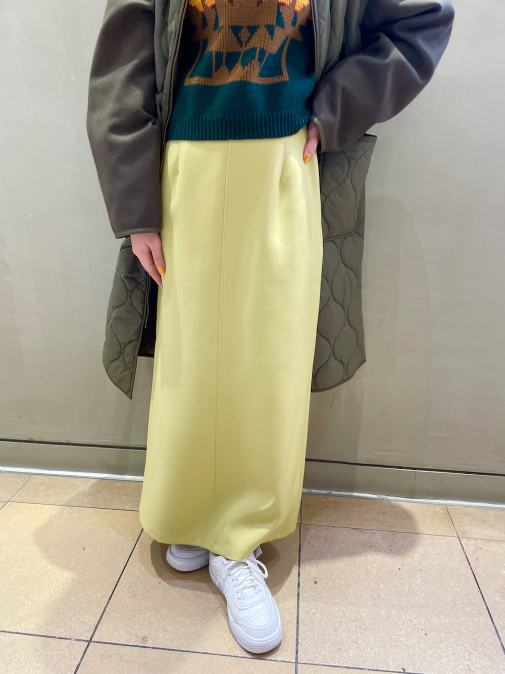 イエロー系のスカート、グリーン系のノーカラーコート、グリーン系のベストを着用したレディースの秋コーディネートの4枚目の写真