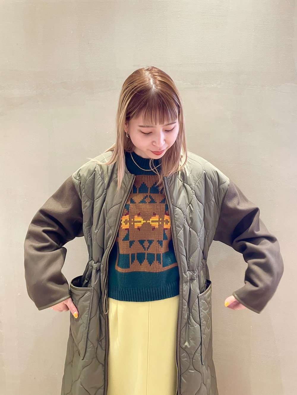 イエロー系のスカート、グリーン系のノーカラーコート、グリーン系のベストを着用したレディースの秋コーディネートの3枚目の写真