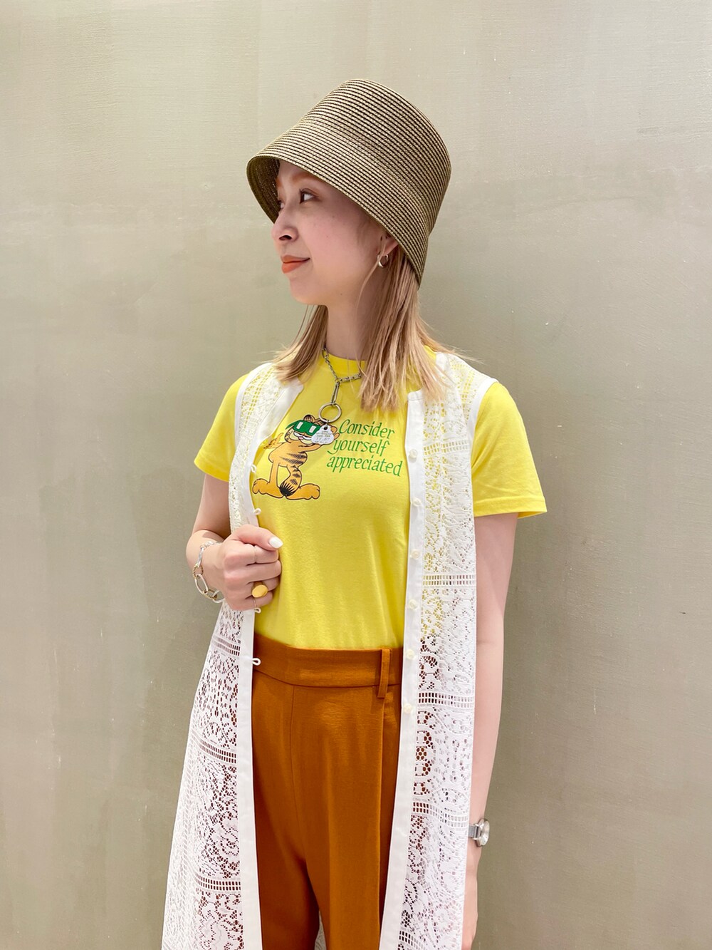 オレンジ系のパンツ、イエロー系のTシャツ/カットソー、ホワイト系のワンピースを着用したレディースの春コーディネートの2枚目の写真