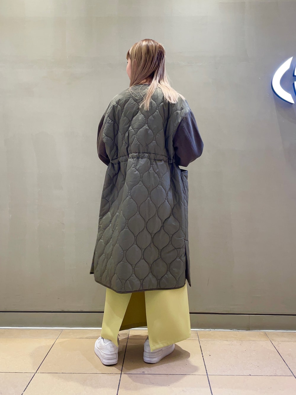 イエロー系のスカート、グリーン系のノーカラーコート、グリーン系のベストを着用したレディースの秋コーディネートの2枚目の写真