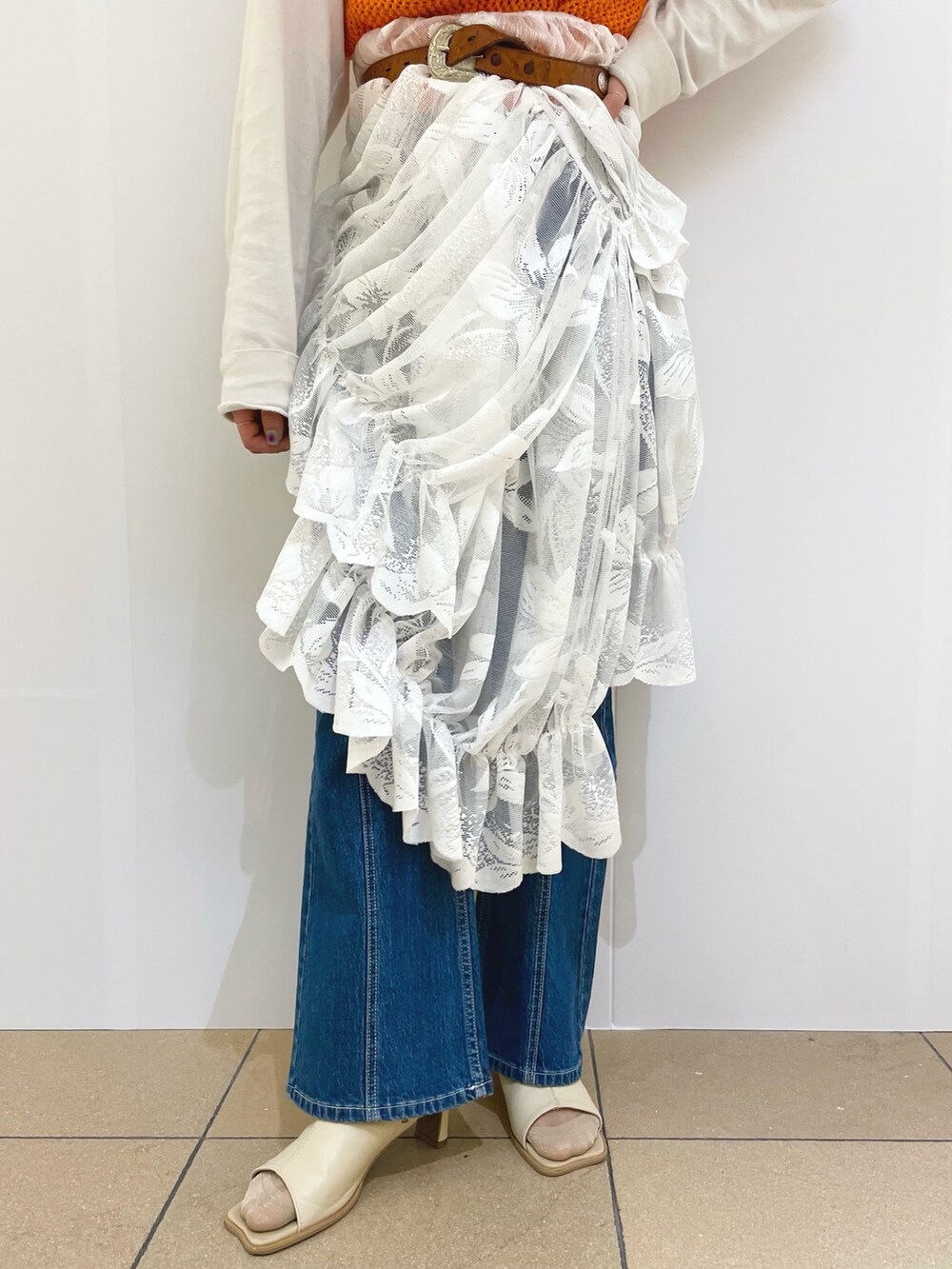 オレンジ系のベスト、ブルー系のデニムパンツ、ホワイト系のサンダルを着用したレディースの春コーディネートの3枚目の写真