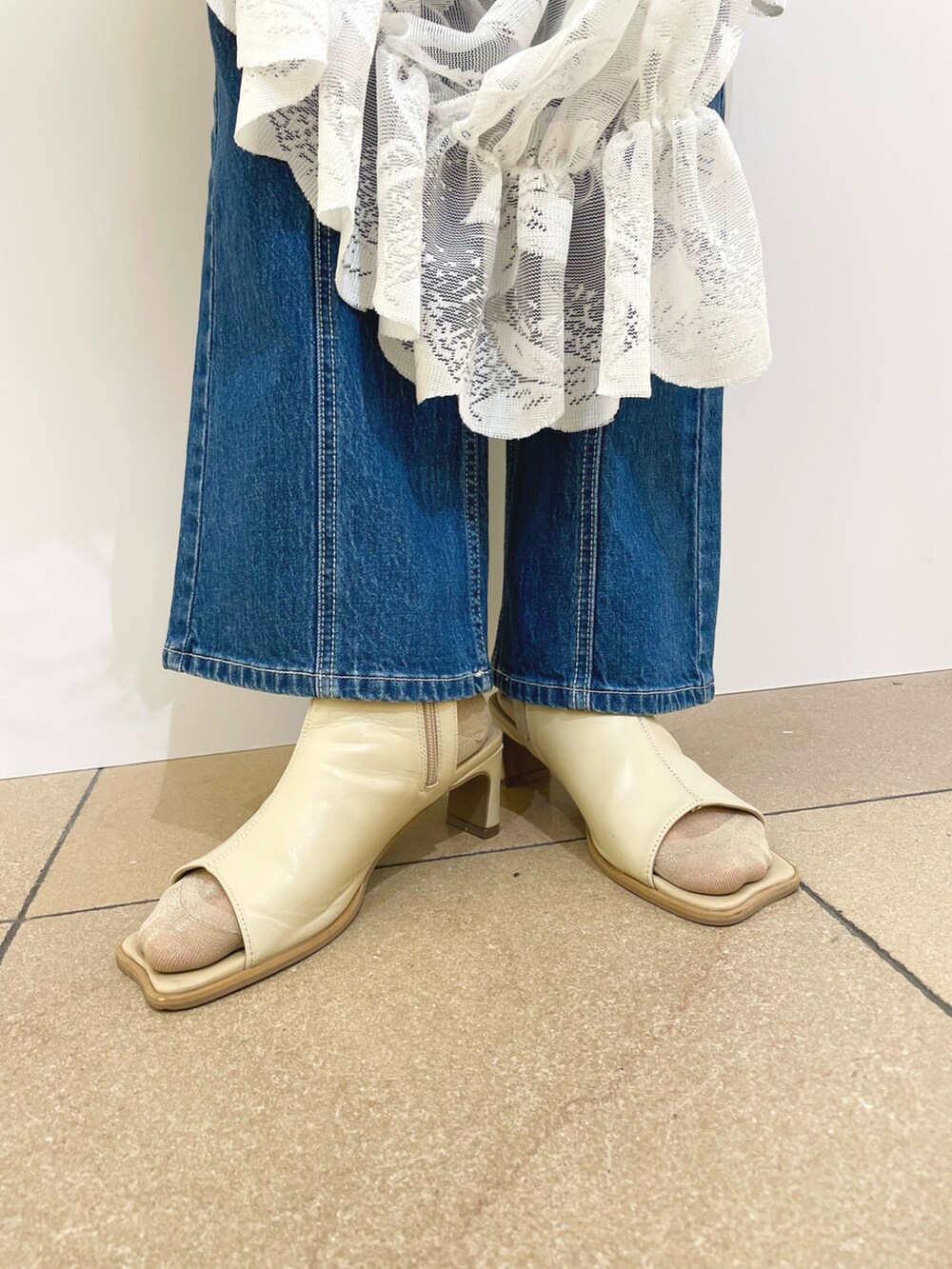 オレンジ系のベスト、ブルー系のデニムパンツ、ホワイト系のサンダルを着用したレディースの春コーディネートの4枚目の写真