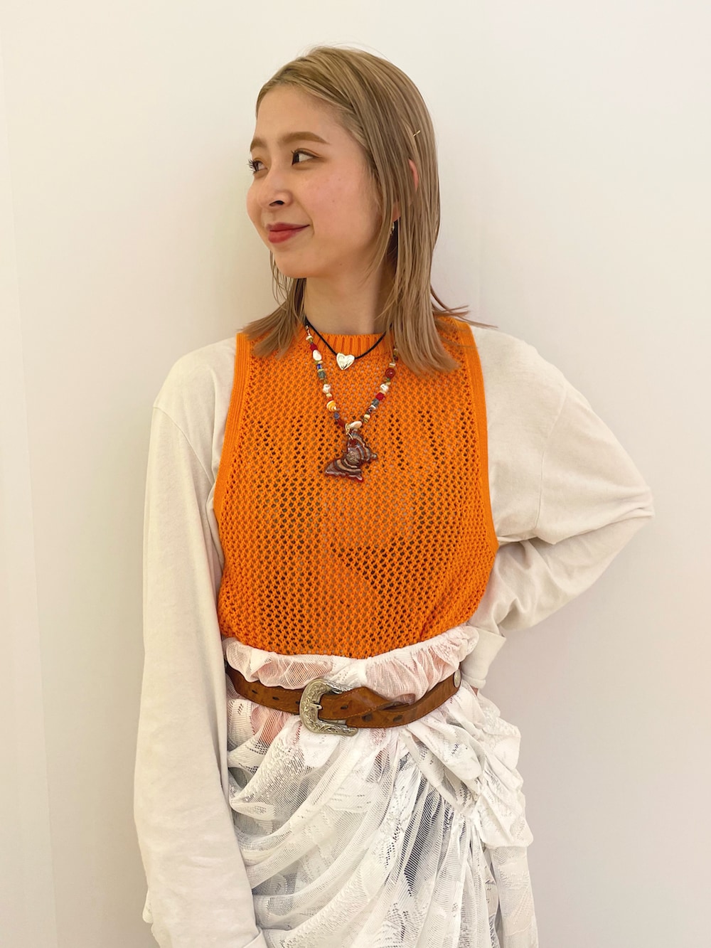 オレンジ系のベスト、ブルー系のデニムパンツ、ホワイト系のサンダルを着用したレディースの春コーディネートの2枚目の写真