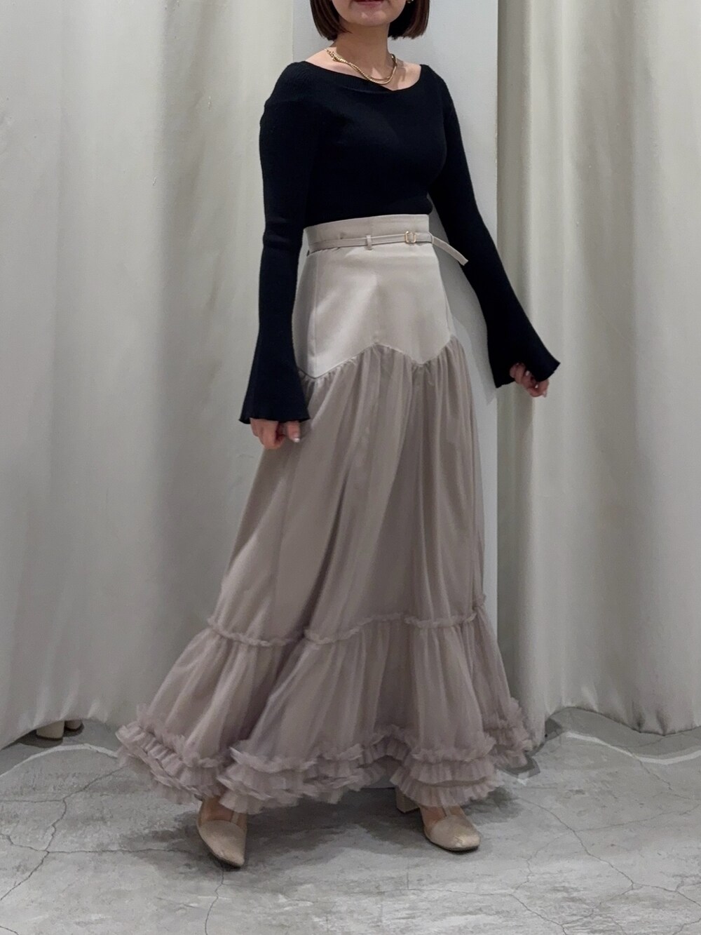 ベージュ系のスカート、ブラック系のニット/セーターを着用したレディースの春コーディネートの2枚目の写真