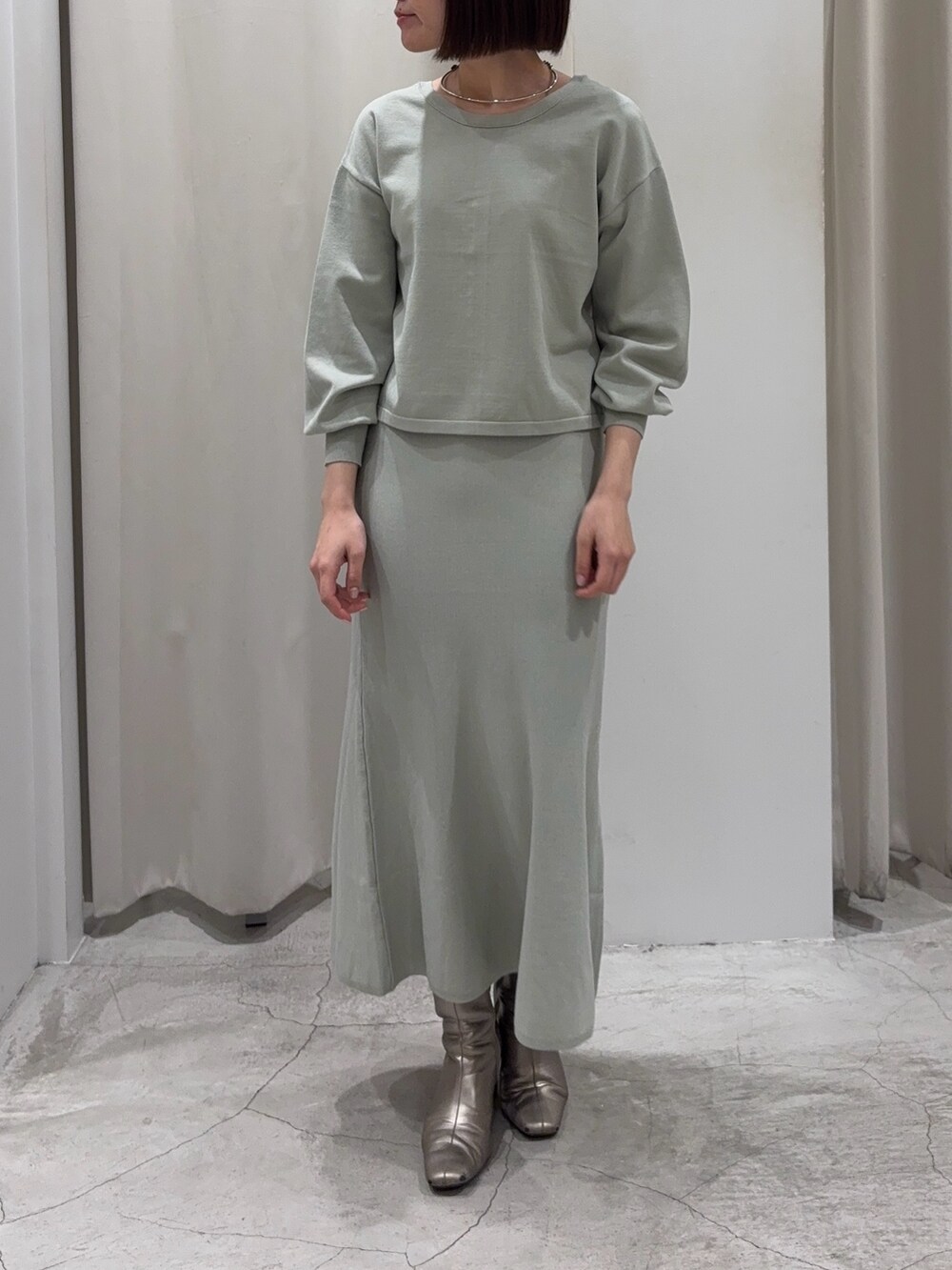 グリーン系のニット/セーター、グリーン系のスカート、シルバー系のブーツを着用したレディースの冬コーディネートの6枚目の写真