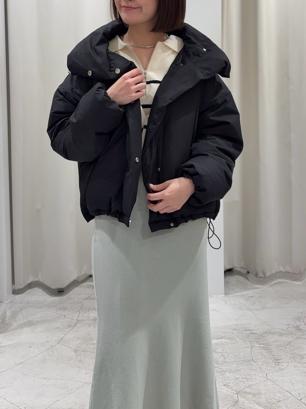 ブラック系のダウンジャケット/コート、ホワイト系のニット/セーター、グリーン系のスカートを着用したレディースの冬コーディネートの3枚目の写真