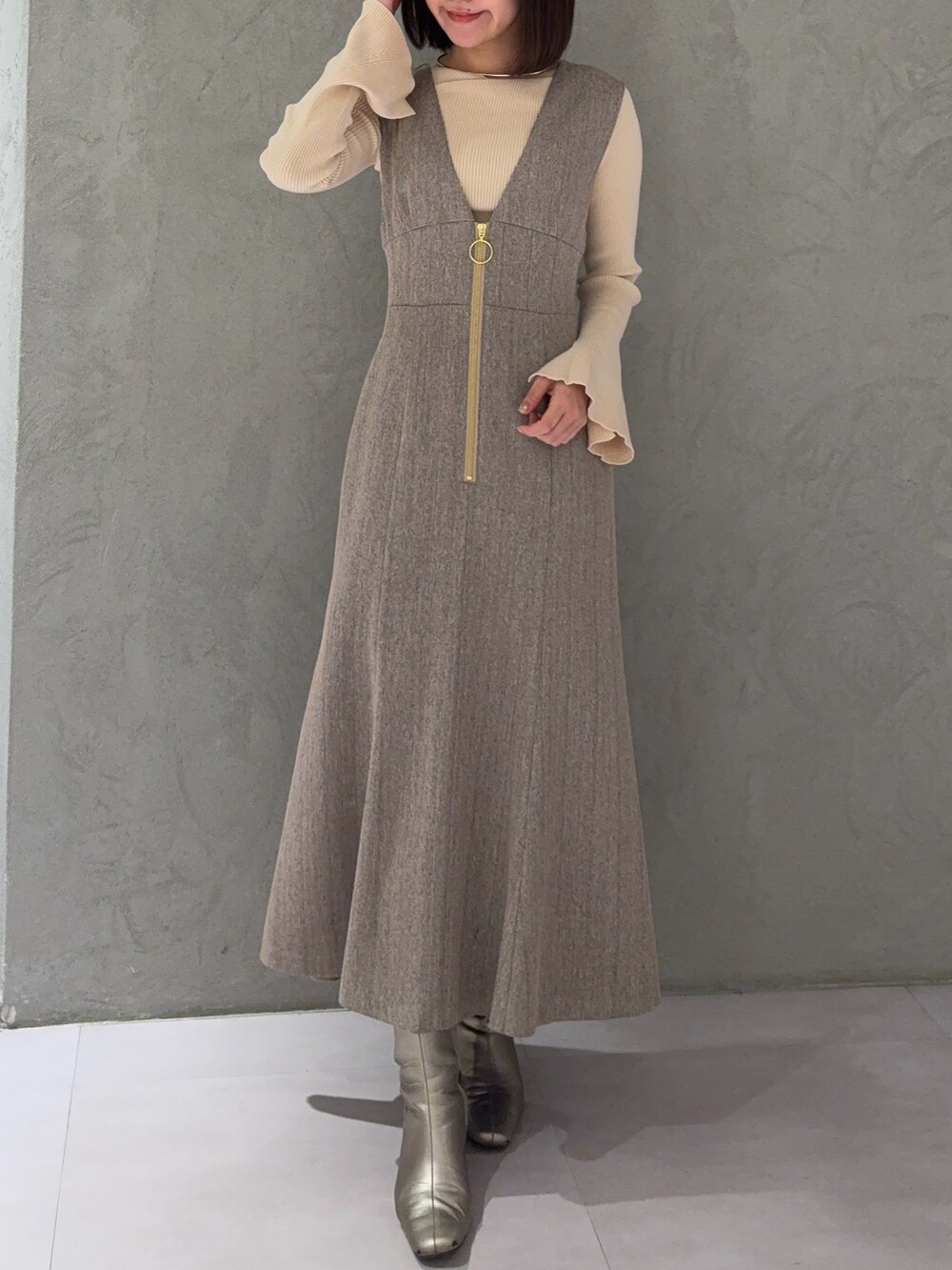 ベージュ系のジャンパースカート、ホワイト系のニット/セーター、シルバー系のブーツを着用したレディースの冬コーディネートの4枚目の写真