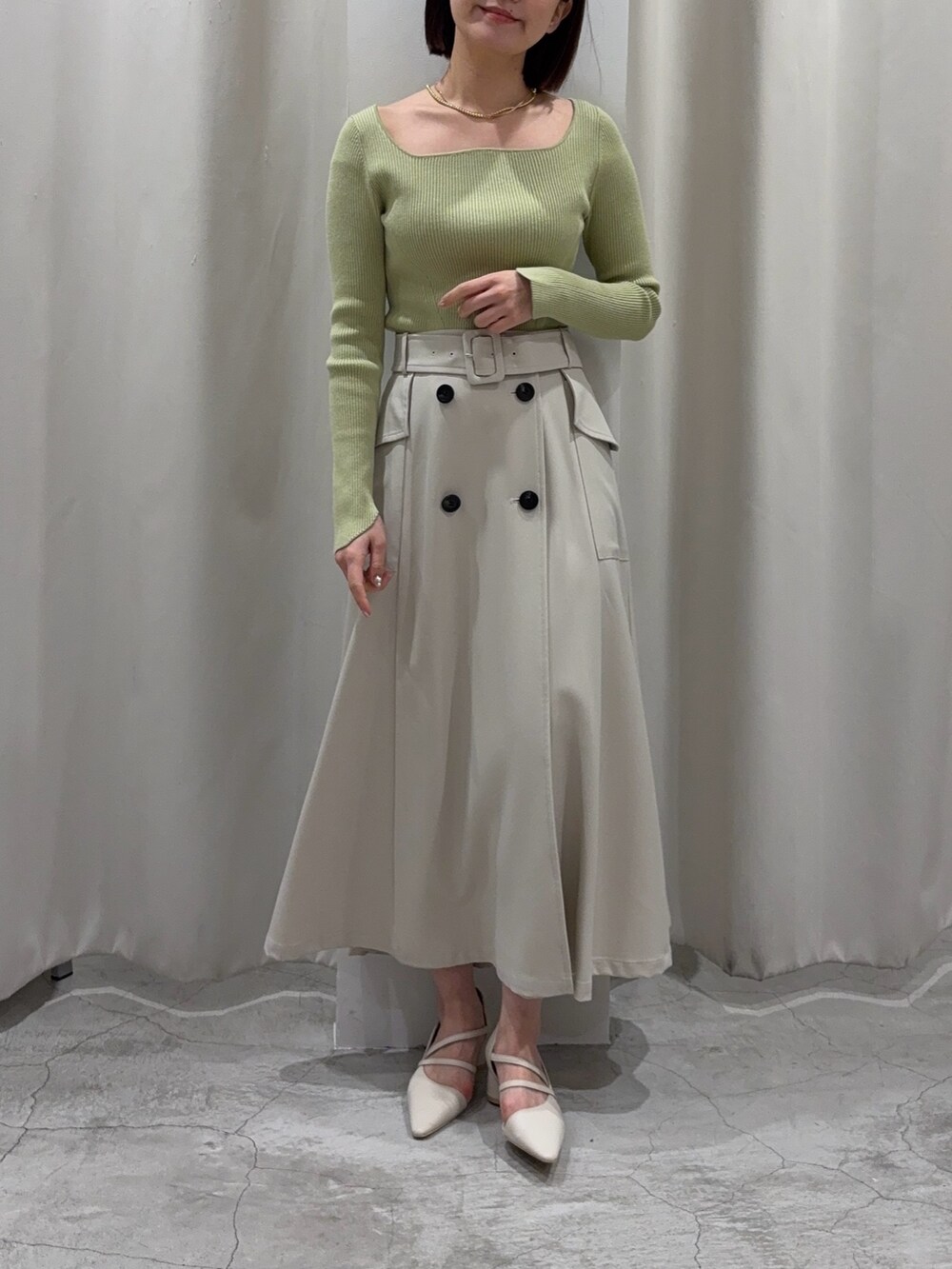 ホワイト系のトレンチコート、グリーン系のニット/セーター、ホワイト系のパンプスを着用したレディースの冬コーディネートの2枚目の写真