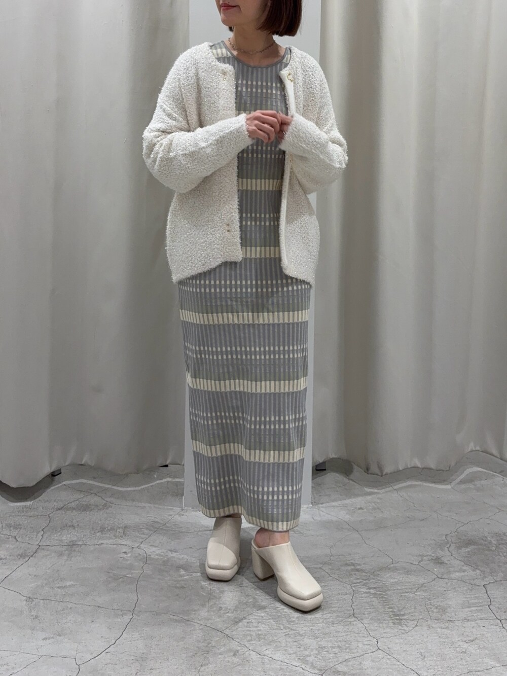 グレー系のワンピース、ホワイト系のカーディガン/ボレロ、ホワイト系のサンダルを着用したレディースの冬コーディネートの6枚目の写真