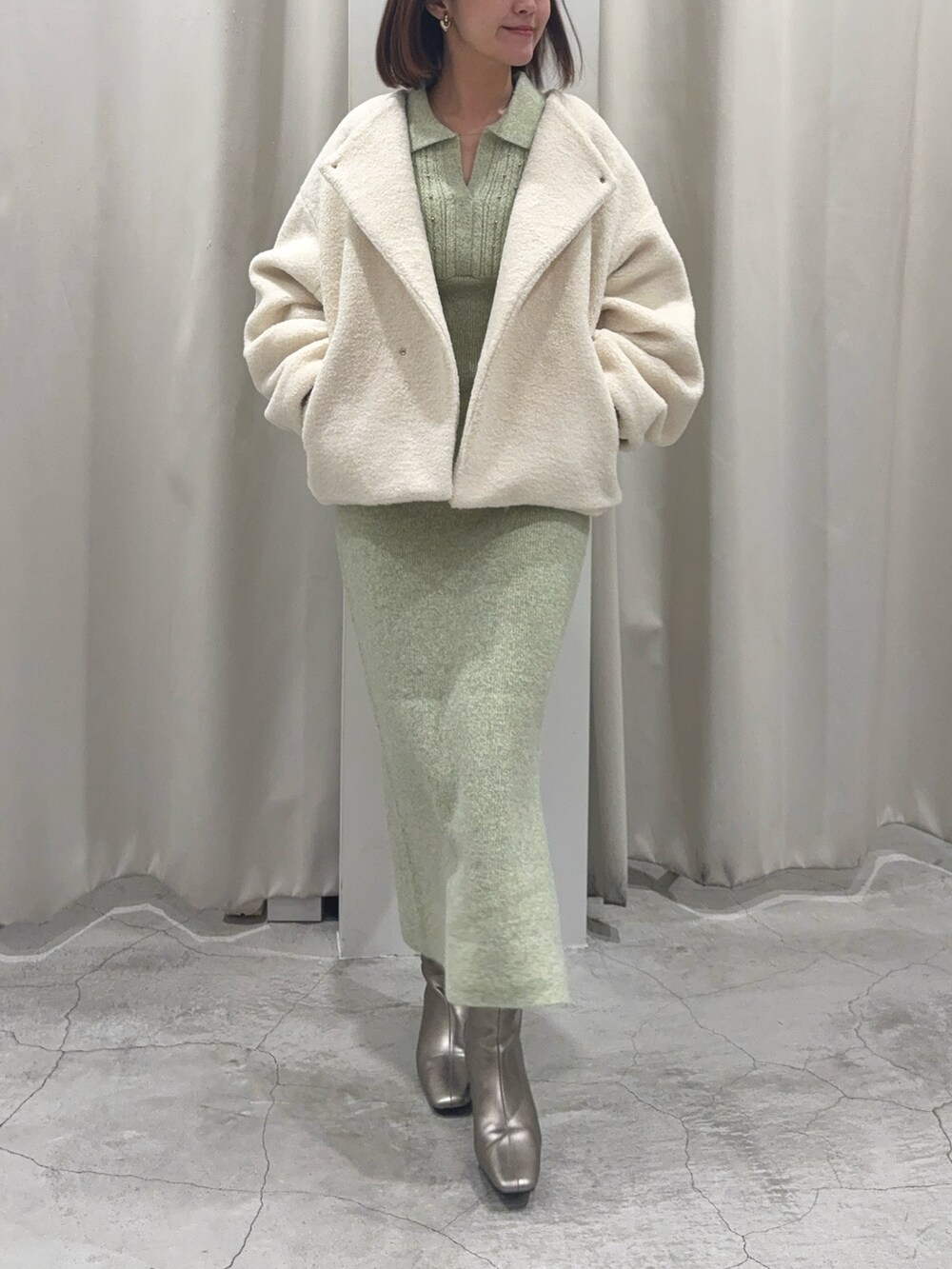 グリーン系のワンピース、シルバー系のブーツ、ゴールド系のイヤリングを着用したレディースの秋コーディネートの6枚目の写真