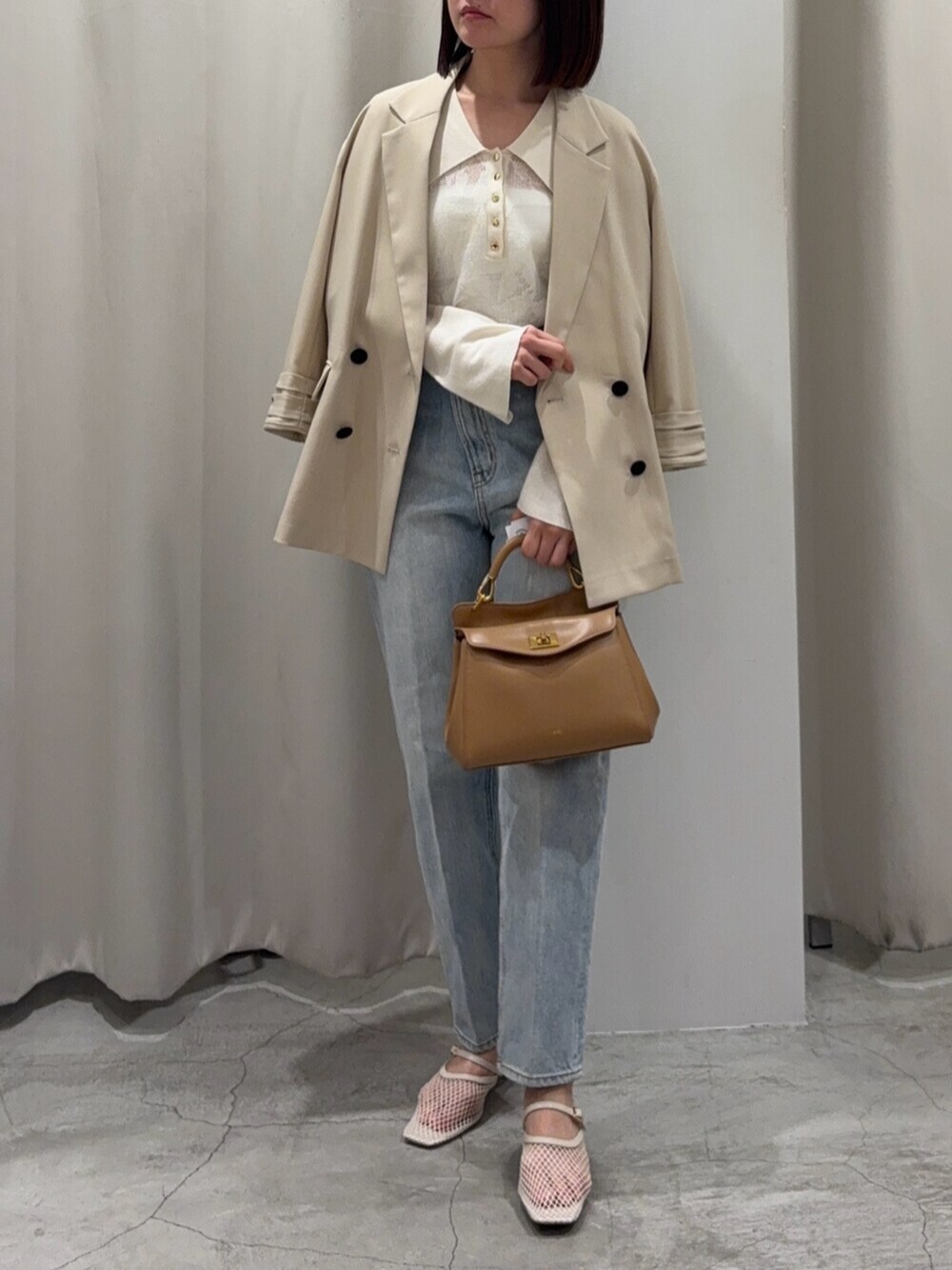 ブルー系のデニムパンツ、ブラウン系のハンドバッグ、ホワイト系のサンダルを着用したレディースの春コーディネートの2枚目の写真