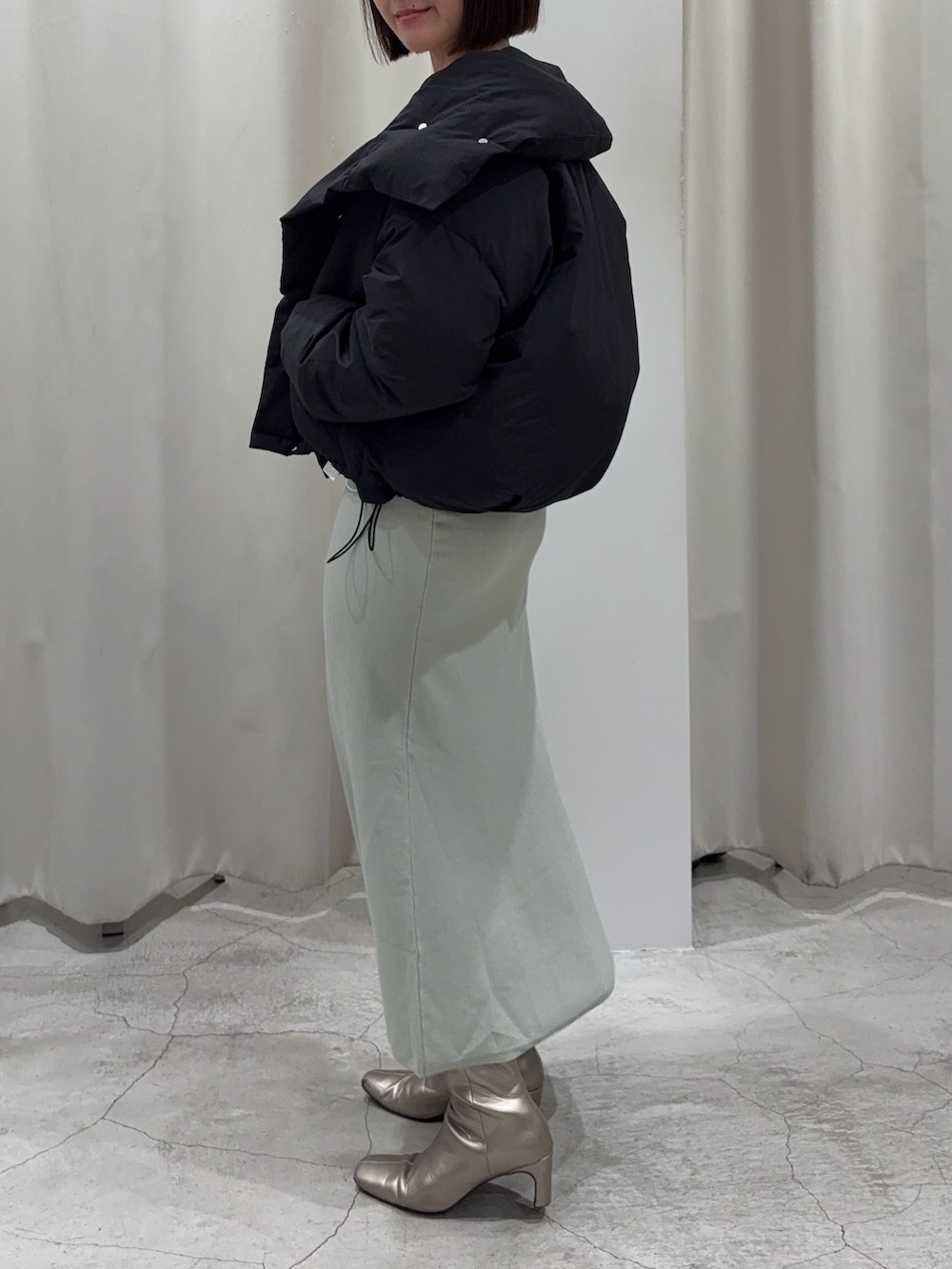 ブラック系のダウンジャケット/コート、ホワイト系のニット/セーター、グリーン系のスカートを着用したレディースの冬コーディネートの2枚目の写真