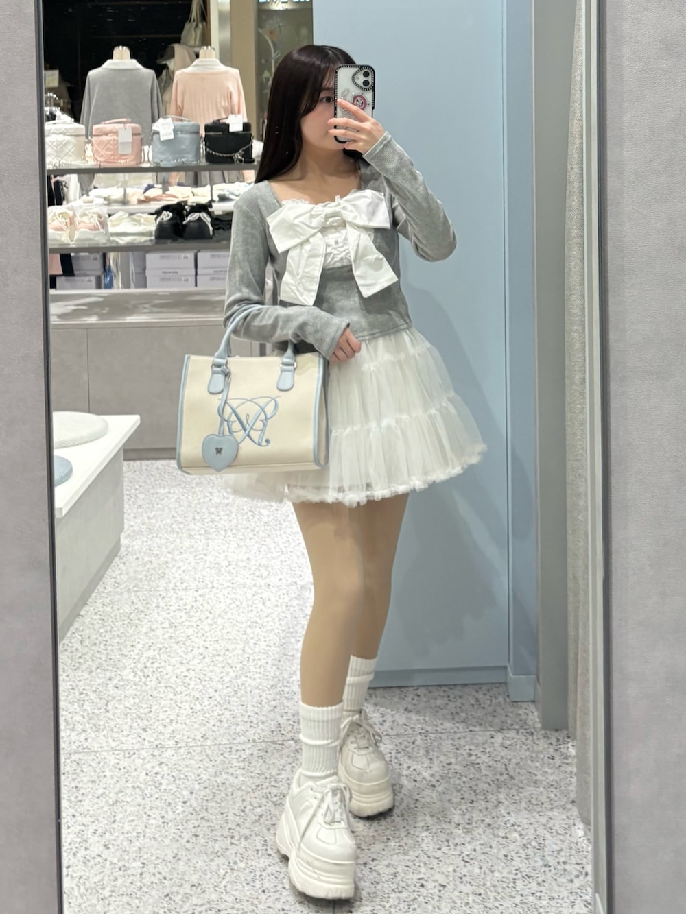 グレー系のTシャツ/カットソー、ブルー系のトートバッグ、ホワイト系のスカートを着用したレディースの冬コーディネートの2枚目の写真