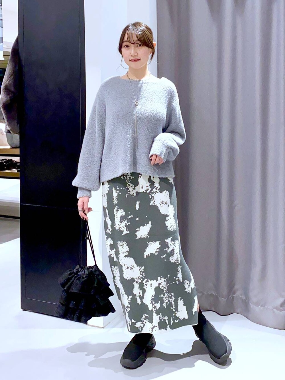 グレー系のスカート、ブラック系のブーツ、ブラック系のショルダーバッグを着用したレディースの秋コーディネートの2枚目の写真