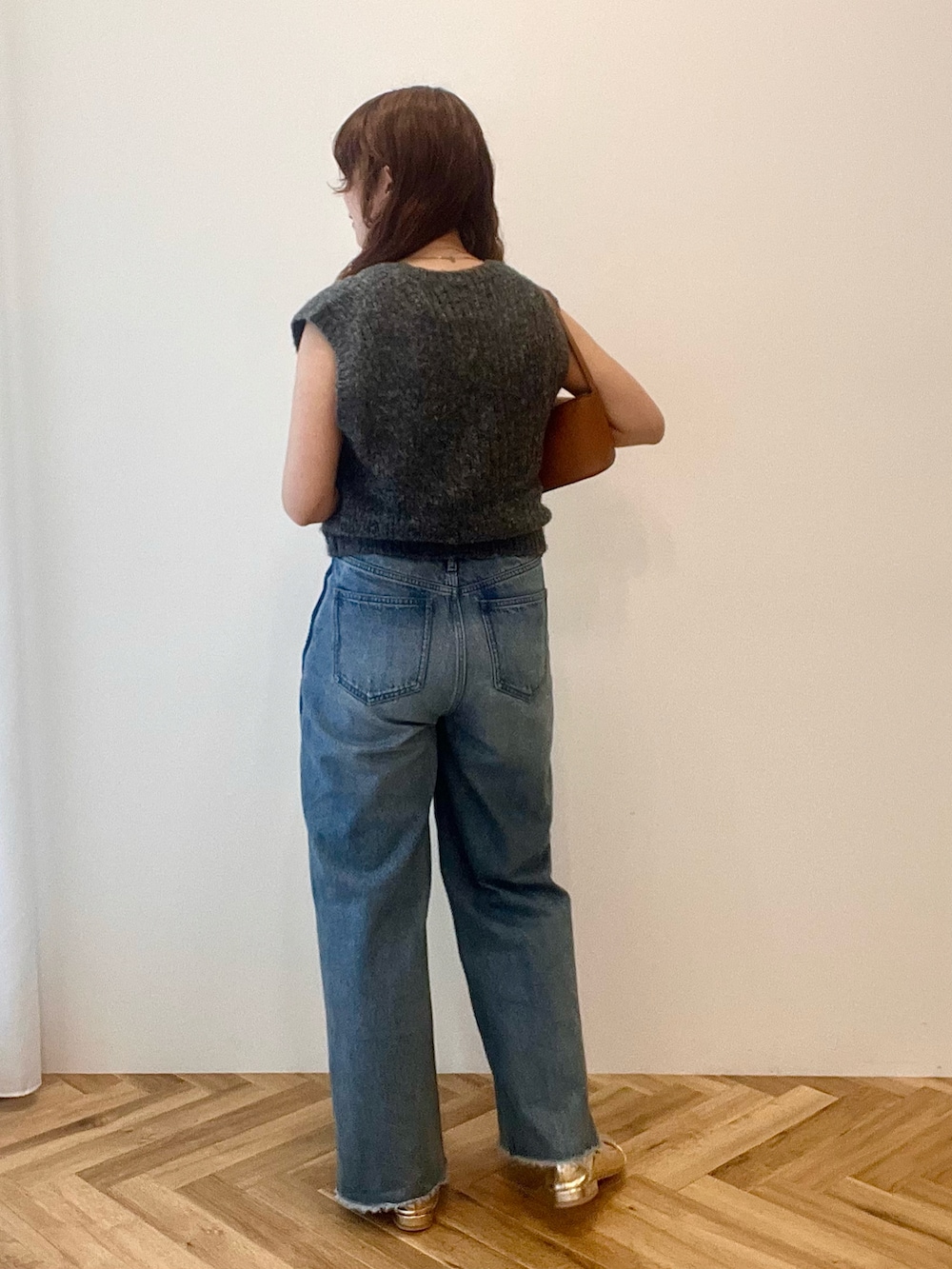 グレー系のベスト、ブルー系のデニムパンツ、ブラウン系のショルダーバッグを着用したレディースの秋コーディネートの3枚目の写真