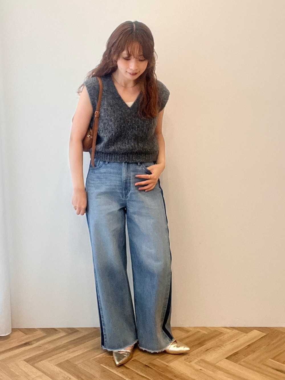 グレー系のベスト、ブルー系のデニムパンツ、ブラウン系のショルダーバッグを着用したレディースの秋コーディネートの2枚目の写真