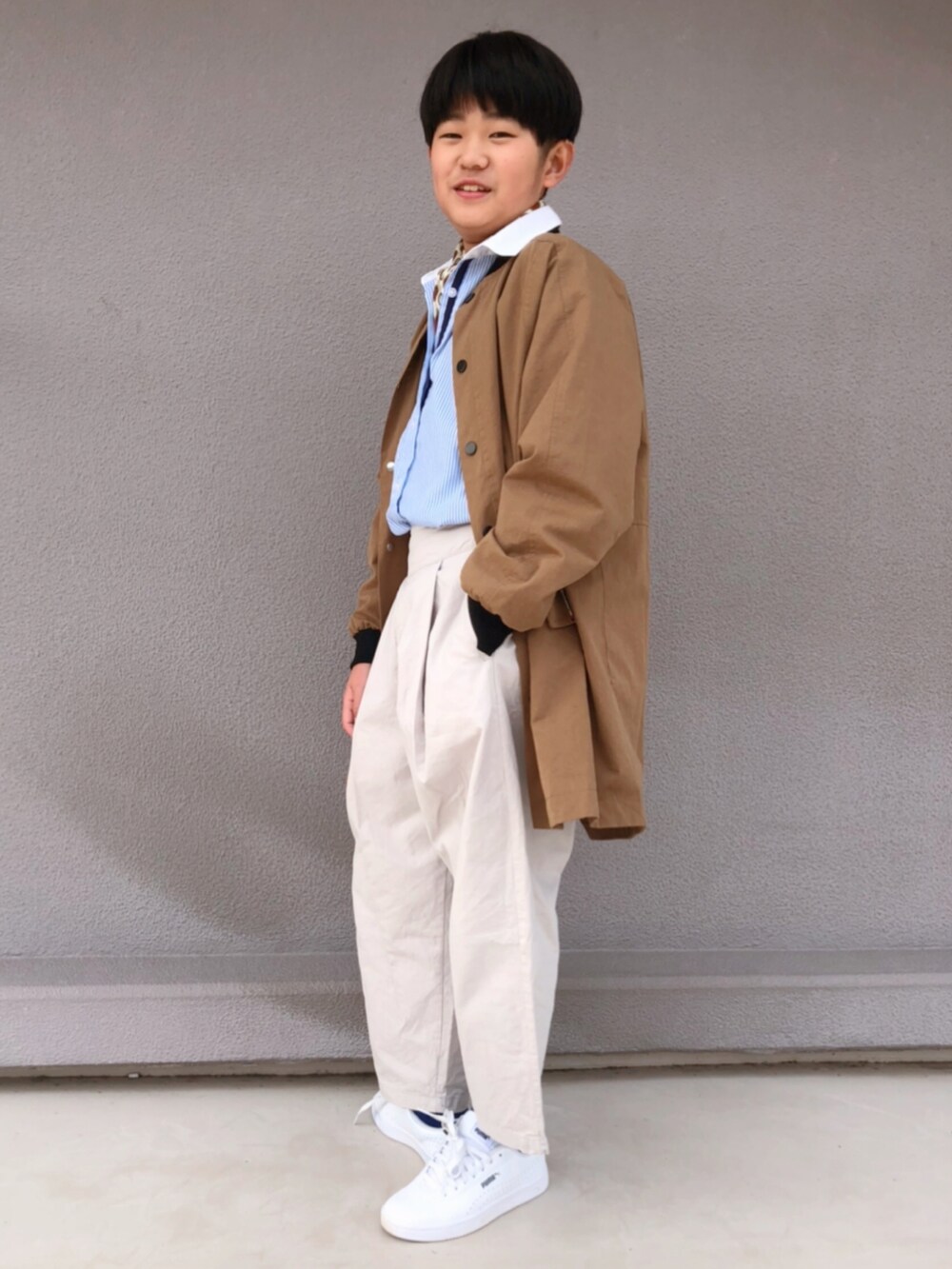 ホワイト系のスラックス、ホワイト系のスニーカー、ベージュ系のノーカラーコートを着用したキッズの春コーディネートの2枚目の写真