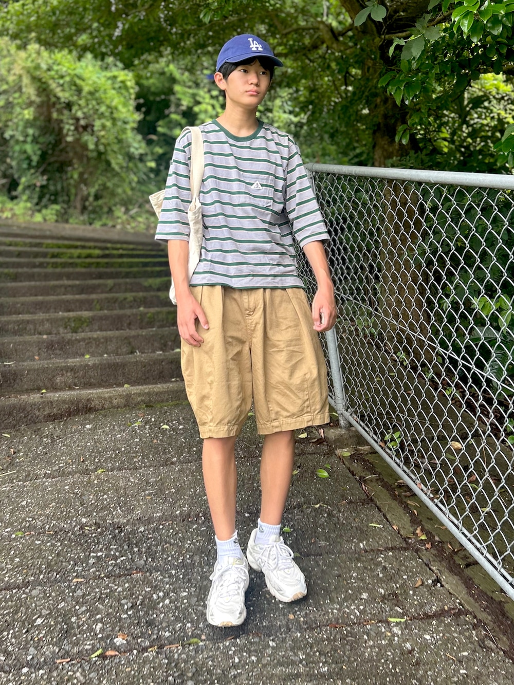 グリーン系のチノパンツ、グレー系のTシャツ/カットソー、ホワイト系のトートバッグを着用したメンズの夏コーディネートの2枚目の写真