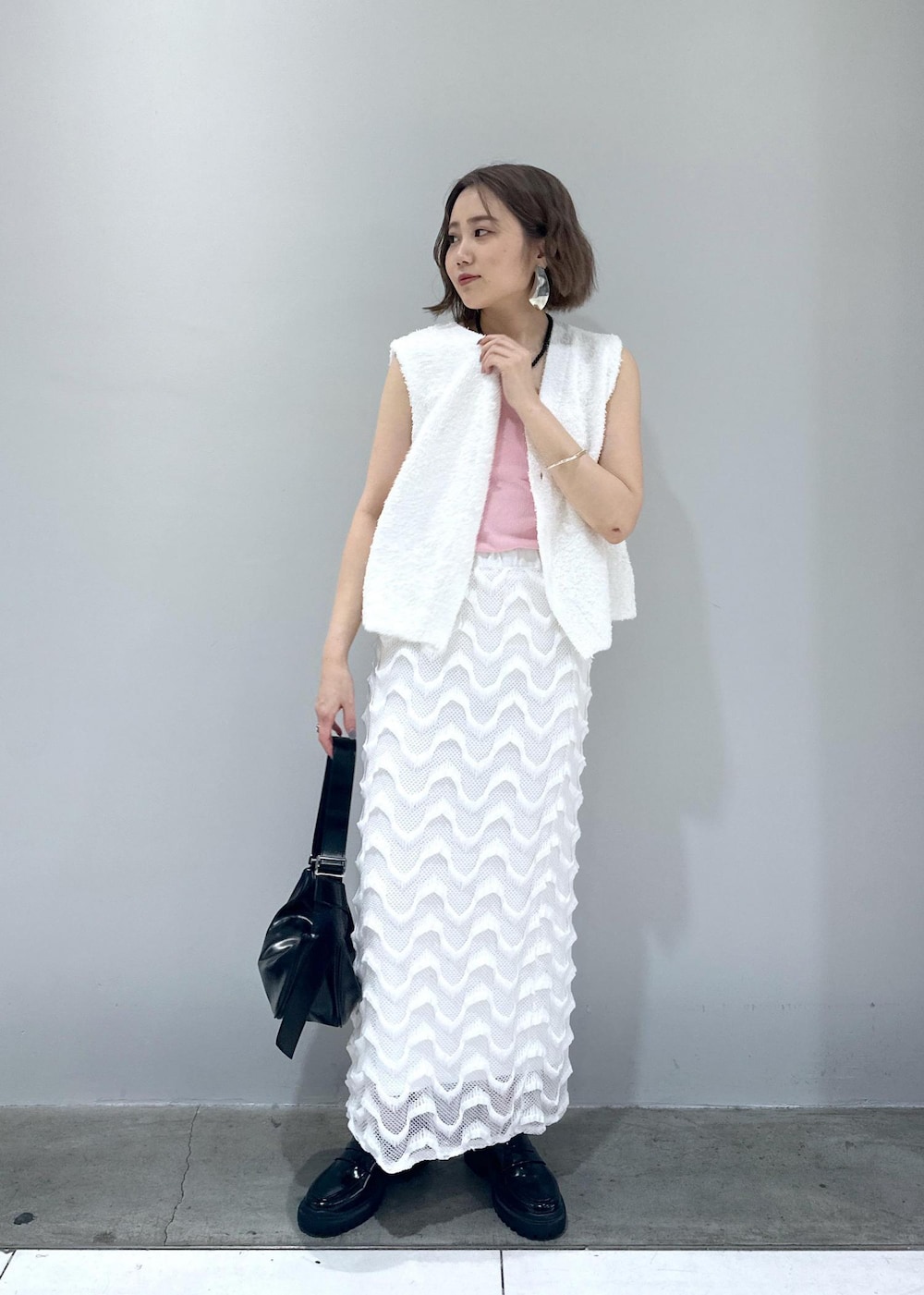 ブラック系のローファー、ブラック系のショルダーバッグ、ホワイト系のベストを着用したレディースの春コーディネートの2枚目の写真