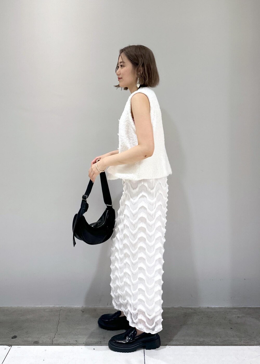 ブラック系のローファー、ブラック系のショルダーバッグ、ホワイト系のベストを着用したレディースの春コーディネートの4枚目の写真