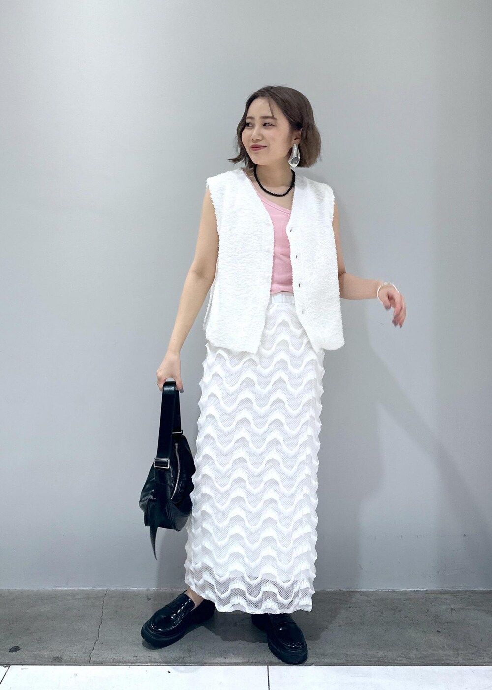 ブラック系のローファー、ブラック系のショルダーバッグ、ホワイト系のベストを着用したレディースの春コーディネートの6枚目の写真