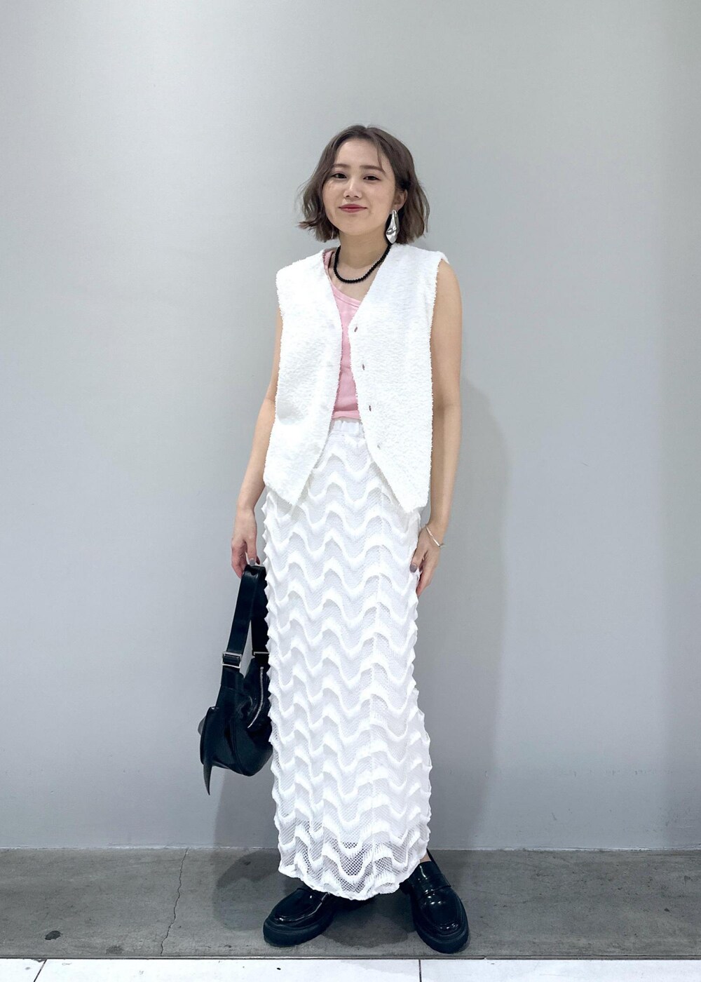 ブラック系のローファー、ブラック系のショルダーバッグ、ホワイト系のベストを着用したレディースの春コーディネートの3枚目の写真