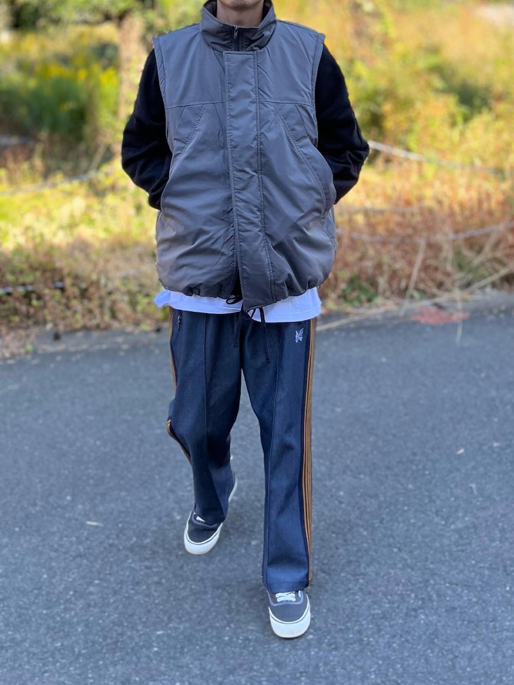 グレー系のダウンベスト、ブラック系のスニーカー、ホワイト系のTシャツ/カットソーを着用したメンズの秋コーディネートの2枚目の写真