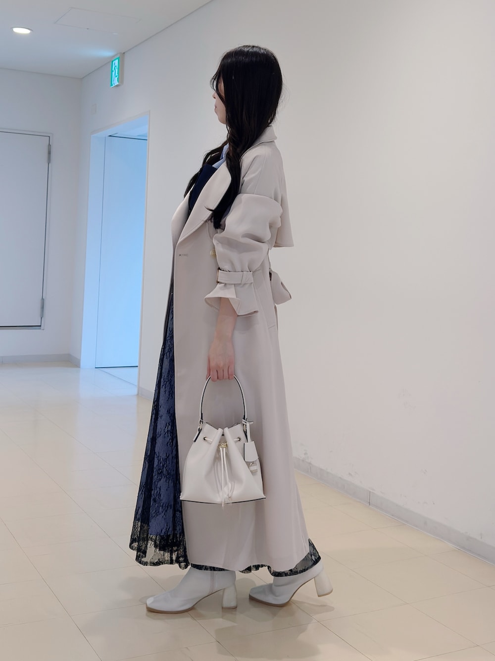 ホワイト系のトレンチコート、ブルー系のワンピース、ホワイト系のブーツを着用したレディースの冬コーディネートの3枚目の写真