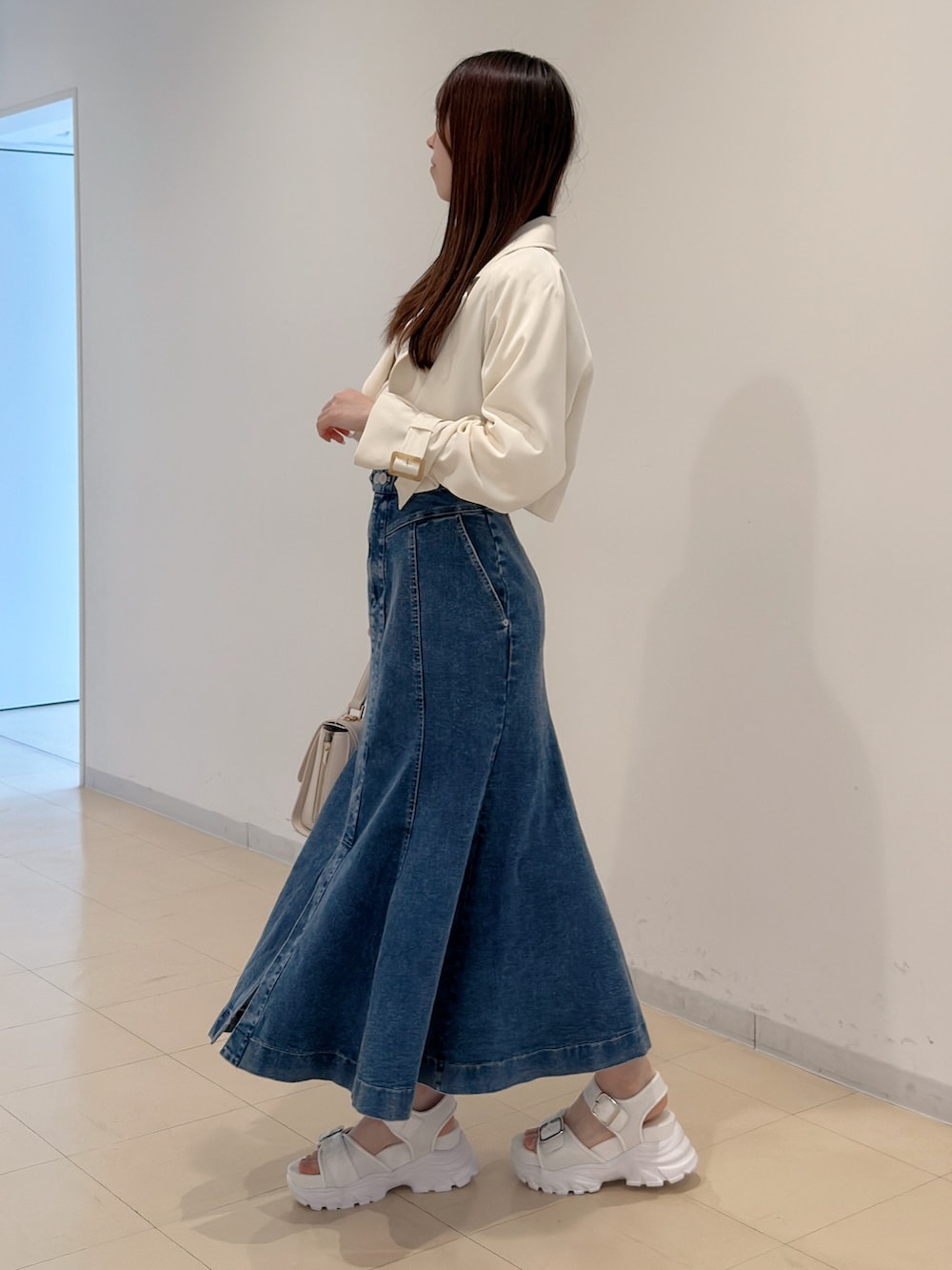 ホワイト系のトレンチコート、ブルー系のスカート、ホワイト系のサンダルを着用したレディースの春コーディネートの3枚目の写真