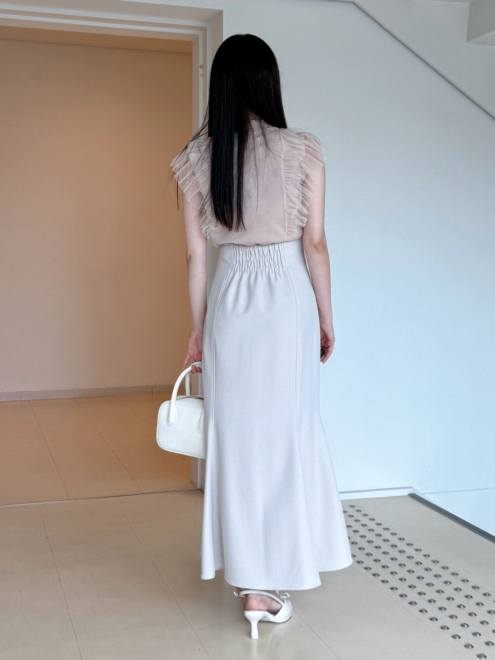 ピンク系のニット/セーター、グレー系のスカート、ホワイト系のハンドバッグを着用したレディースの夏コーディネートの4枚目の写真