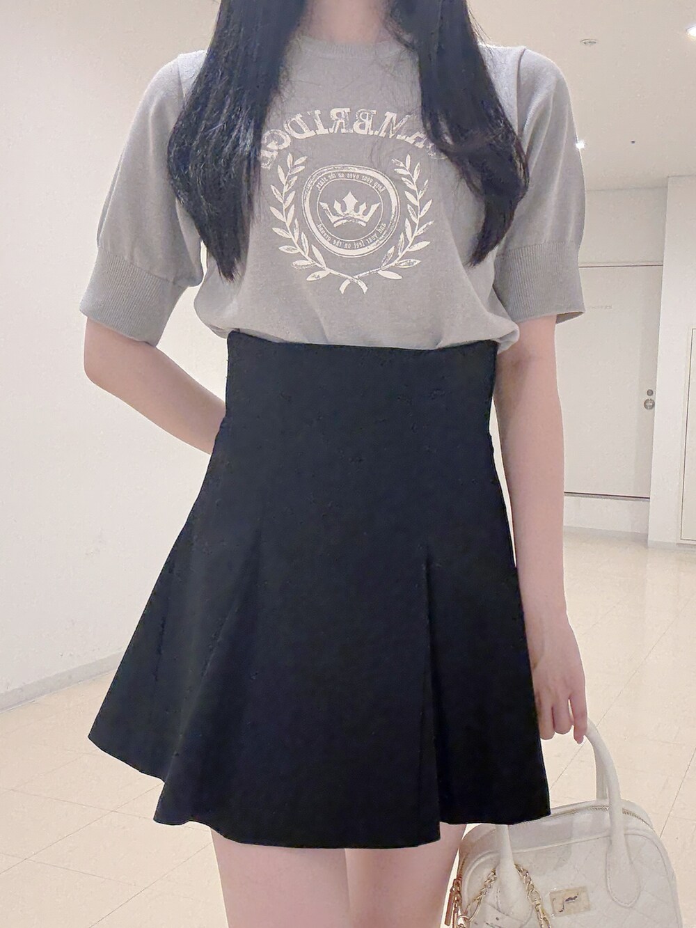 グレー系のニット/セーター、ブラック系のスカート、ホワイト系のハンドバッグを着用したレディースの秋コーディネートの6枚目の写真