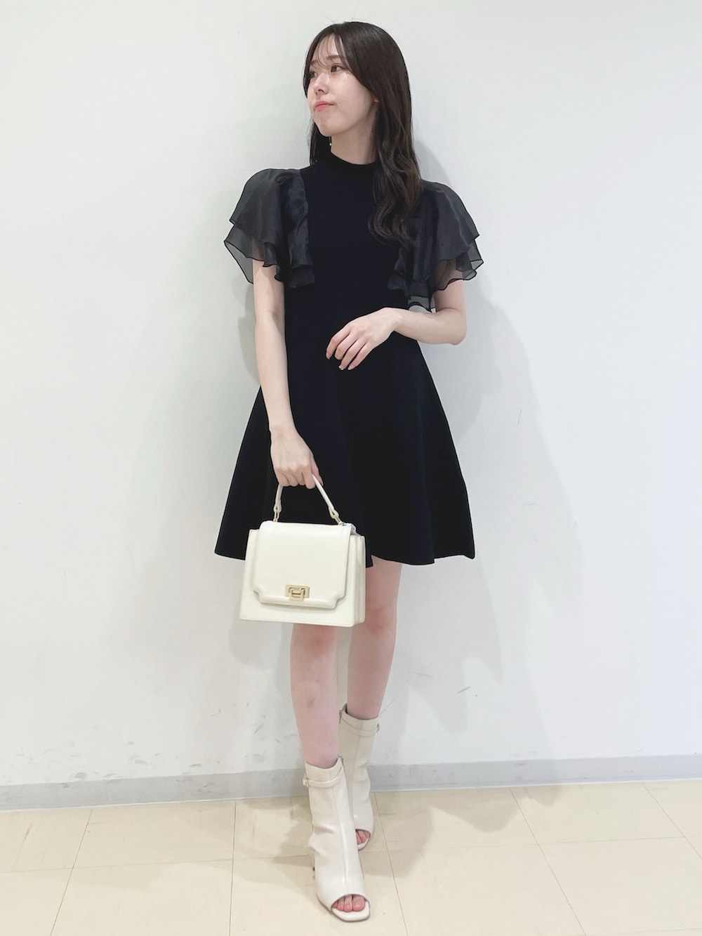 ブラック系のワンピース、ホワイト系のハンドバッグ、ホワイト系のブーツを着用したレディースの春コーディネートの2枚目の写真