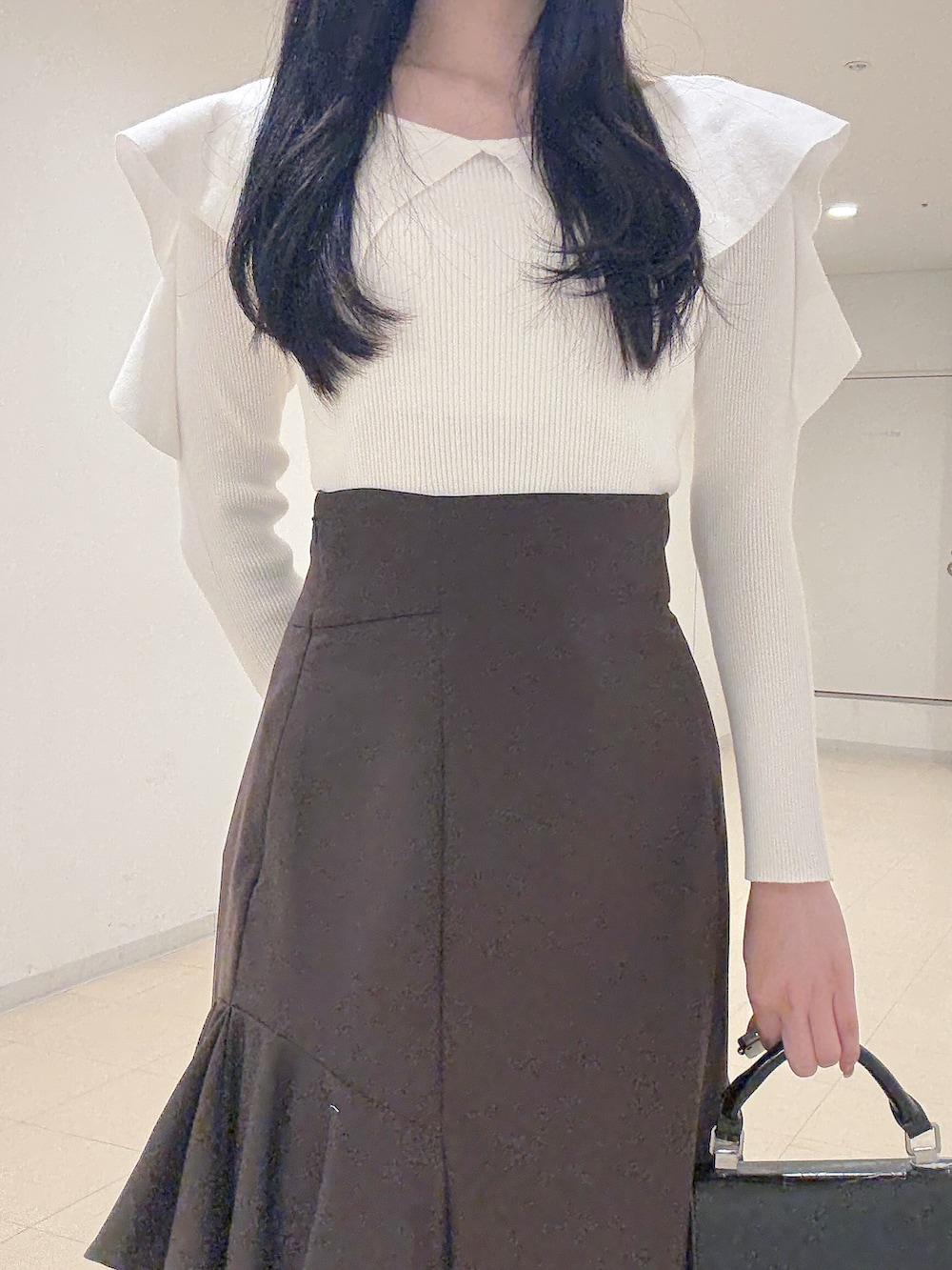 ホワイト系のニット/セーター、ブラウン系のスカート、ブラック系のハンドバッグを着用したレディースの秋コーディネートの6枚目の写真