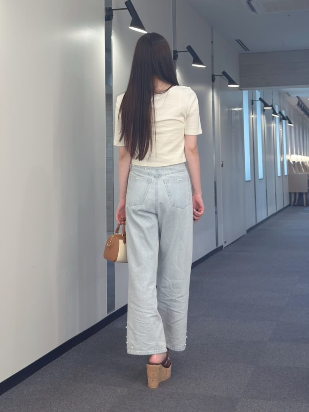 ブラウン系のハンドバッグ、ブラウン系のサンダル、ブルー系のデニムパンツを着用したレディースの夏コーディネートの5枚目の写真