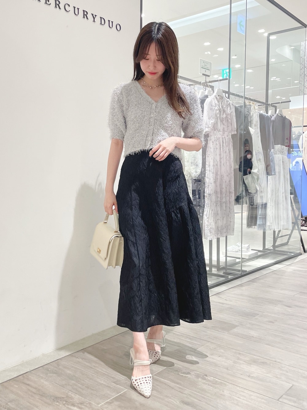 ブラック系のスカート、ホワイト系のパンプス、ホワイト系のカーディガン/ボレロを着用したレディースの冬コーディネートの2枚目の写真