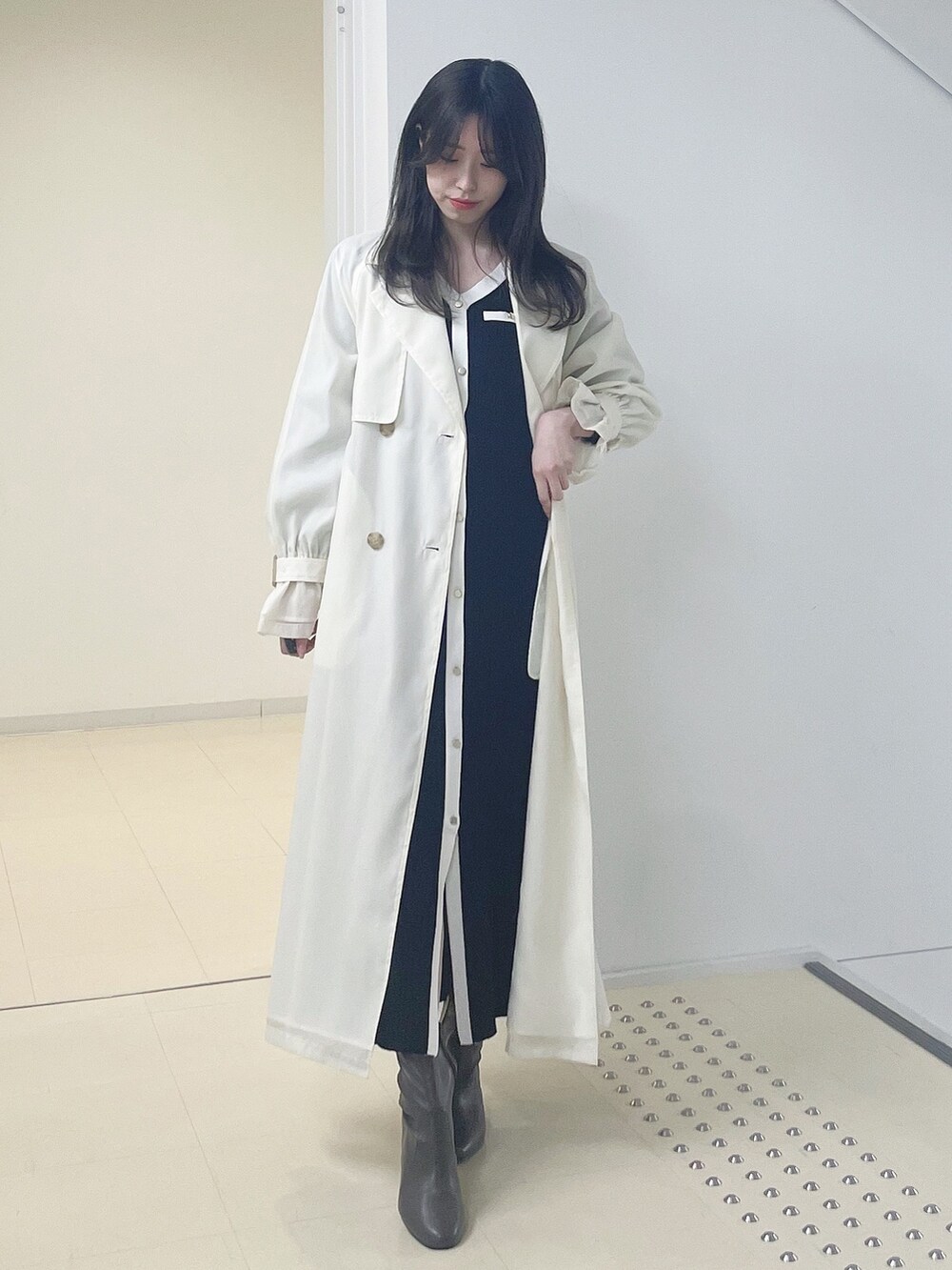 ホワイト系のトレンチコート、ブラック系のワンピース、ブラウン系のブーツを着用したレディースの冬コーディネートの3枚目の写真