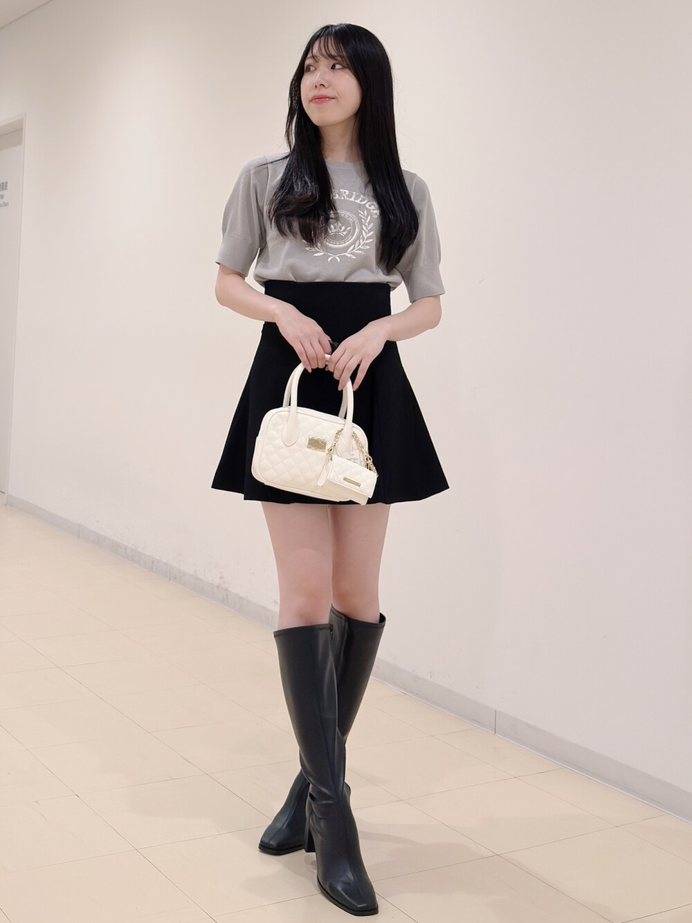 グレー系のニット/セーター、ブラック系のスカート、ホワイト系のハンドバッグを着用したレディースの秋コーディネートの5枚目の写真