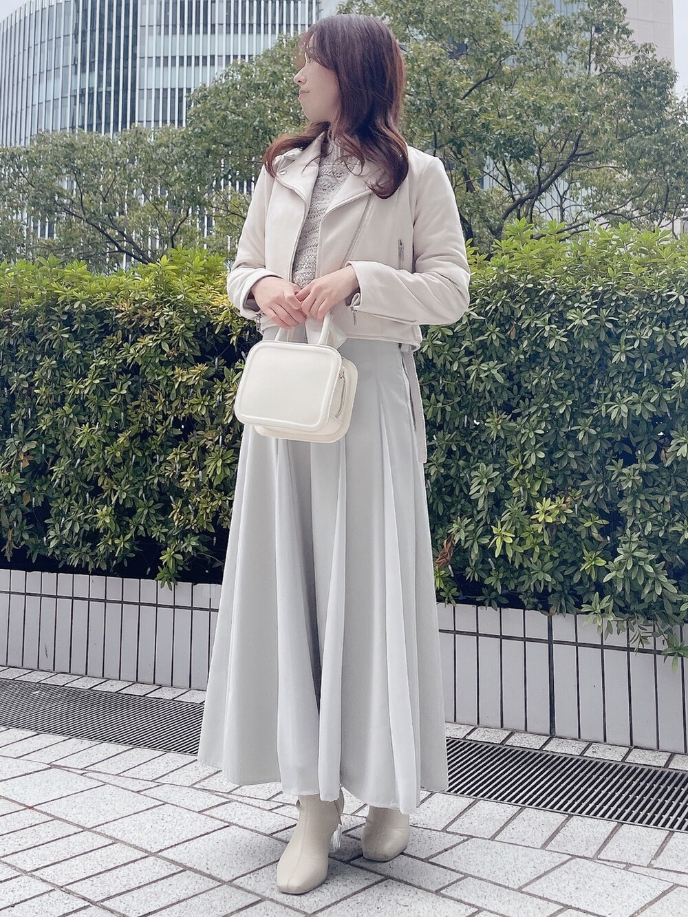 ピンク系のライダースジャケット、グレー系のニット/セーター、グリーン系のスカートを着用したレディースの冬コーディネートの2枚目の写真