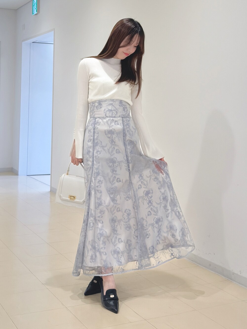 ホワイト系のニット/セーター、ブルー系のスカート、ホワイト系のハンドバッグを着用したレディースの冬コーディネートの2枚目の写真
